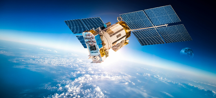 Satellite orbiting Earth with solar panels extended, above clouds and atmosphere, with the moon in background.