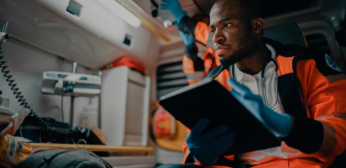 Emergency medical worker in ambulance using tablet with medical equipment.
