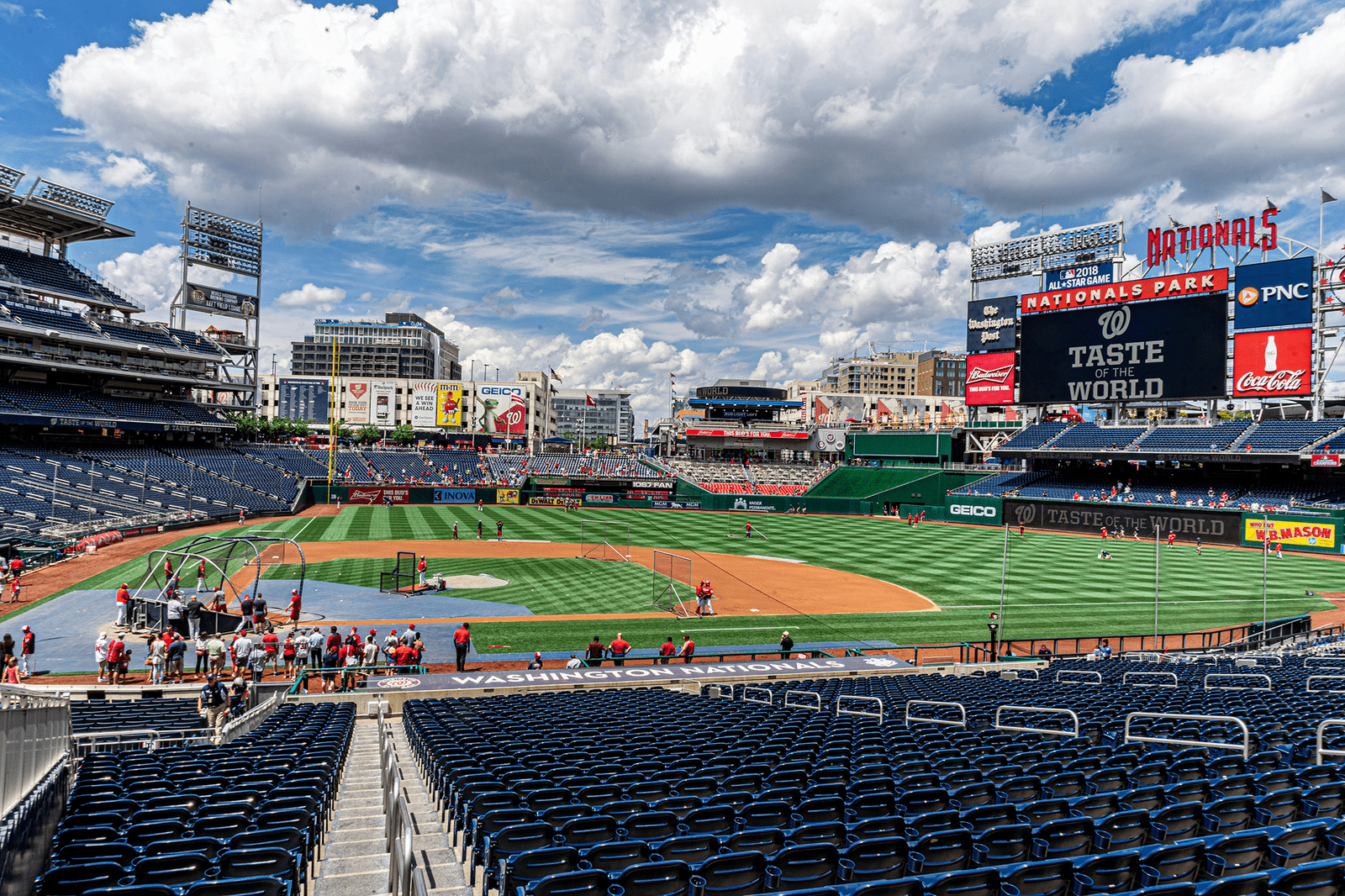 Nationals Park stadium with players on the field and digital screens displaying event messages under a partly cloudy sky.
