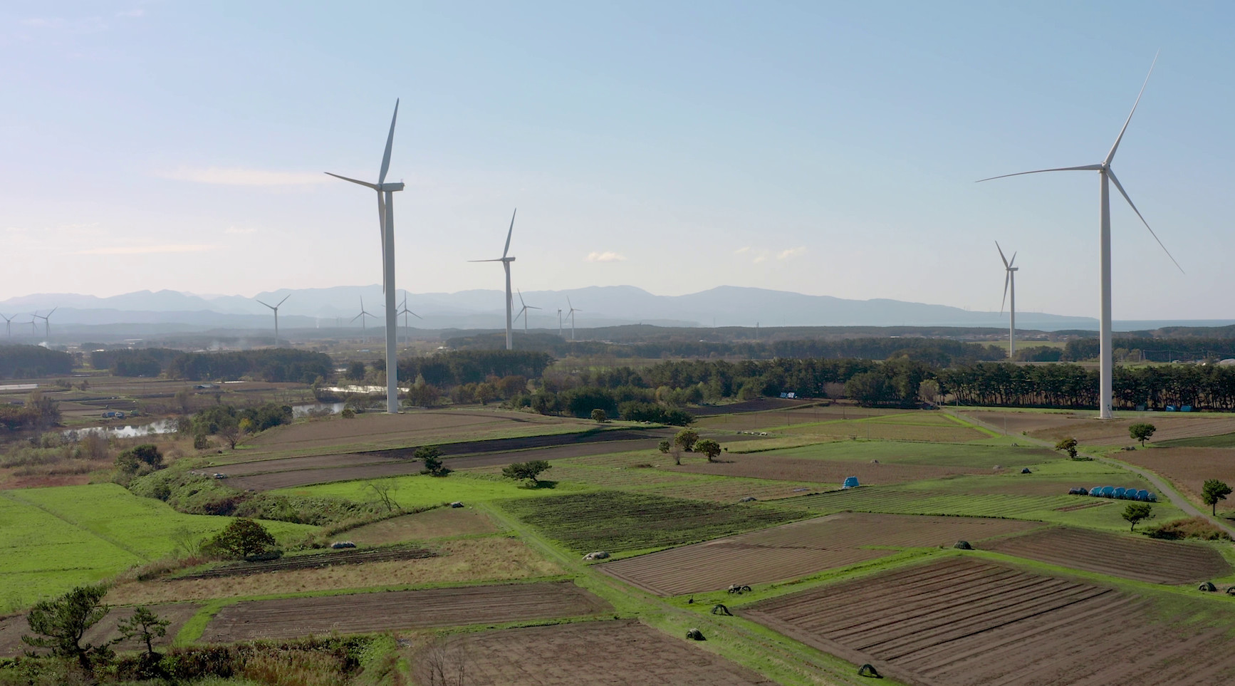 Wind turbines in a rural landscape with mountains in the background.