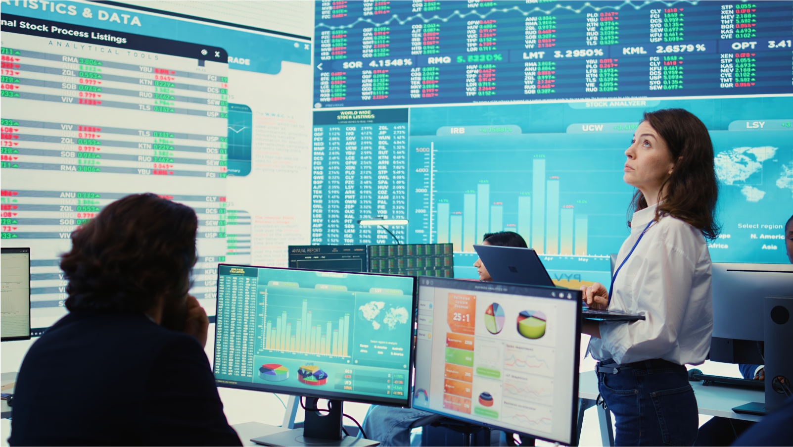Busy trading room with multiple monitors displaying financial data, stock performance, and market analytics.