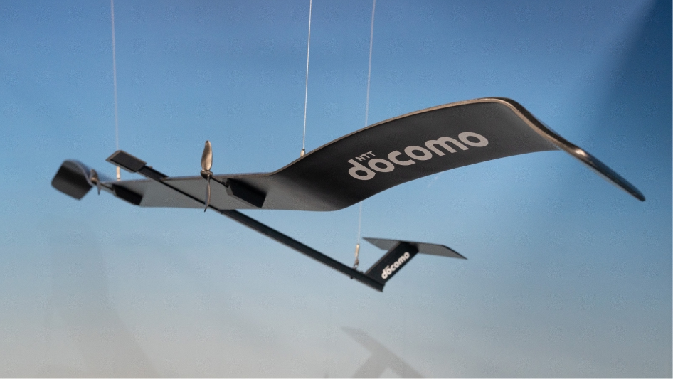 Futuristic black aircraft model labeled 'NTT docomo' suspended against a blue gradient background.