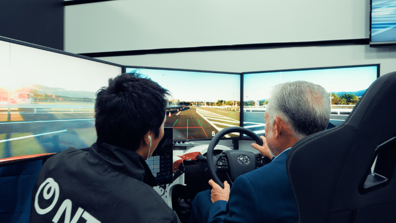 An attendee at the NTT R&D Forum testing the remote mobility exhibit, driving a real car located 80km away from there.